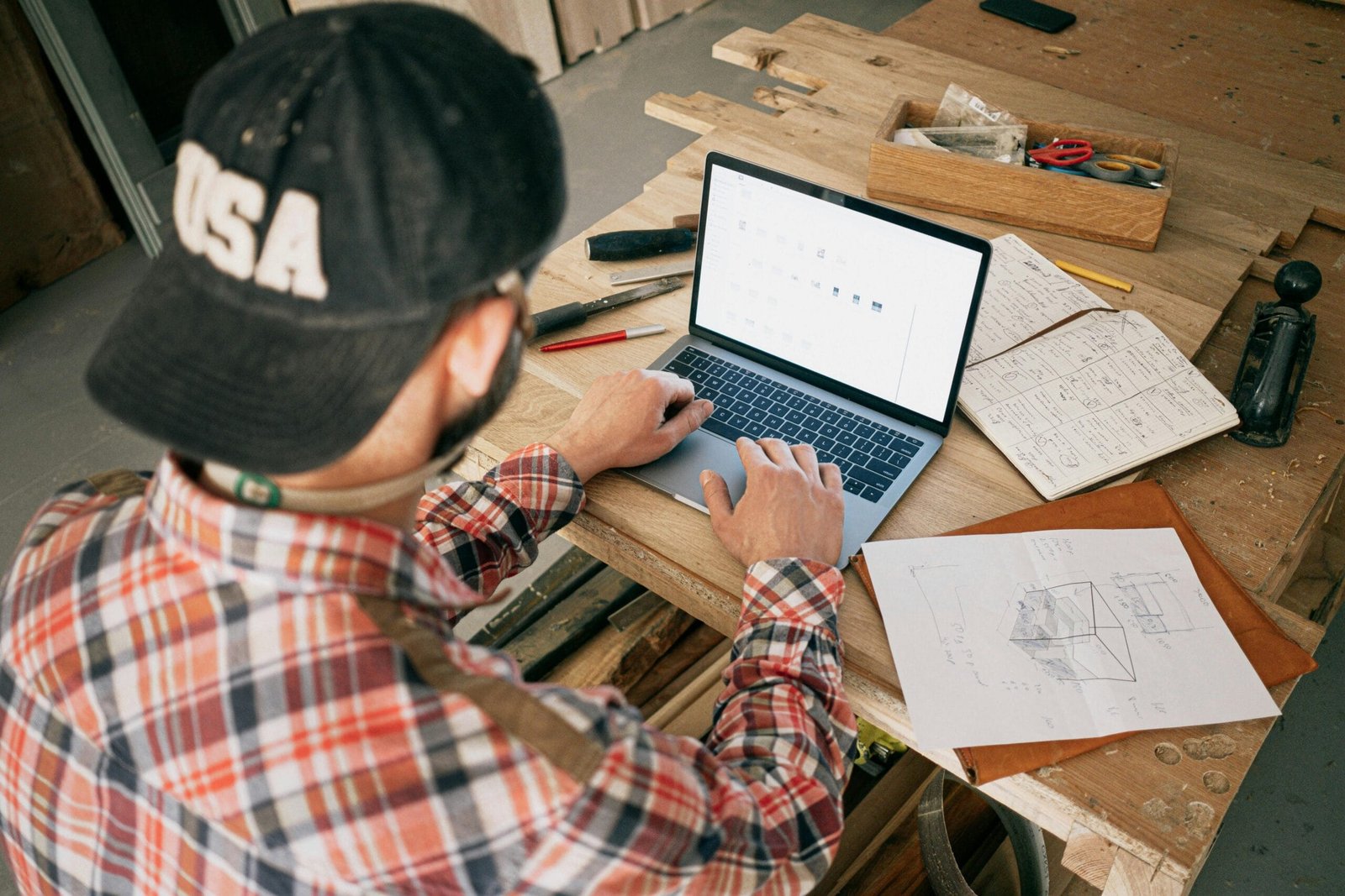 A woodworker in a workshop uses a laptop for furniture design planning and project management.
